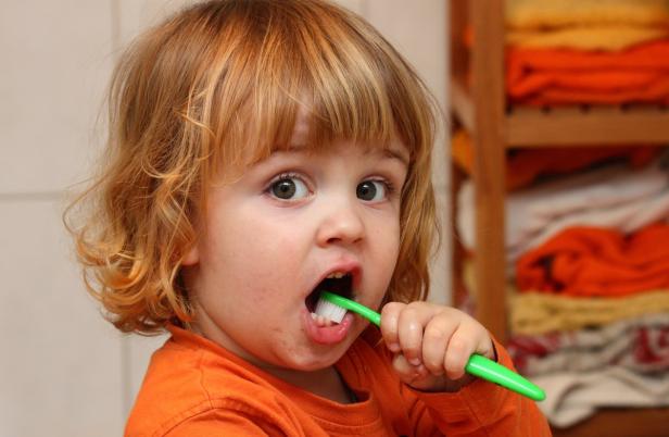 Ein kleines Kind mit blonden Haaren putzt sich die Zähne.