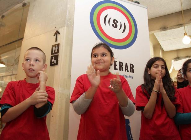 Eine Gruppe Kinder in roten T-Shirts steht vor einem Banner und klatscht in die Hände.