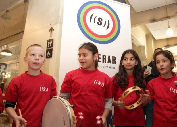 Eine Gruppe Kinder in roten T-Shirts musiziert mit Trommeln und Tamburinen.