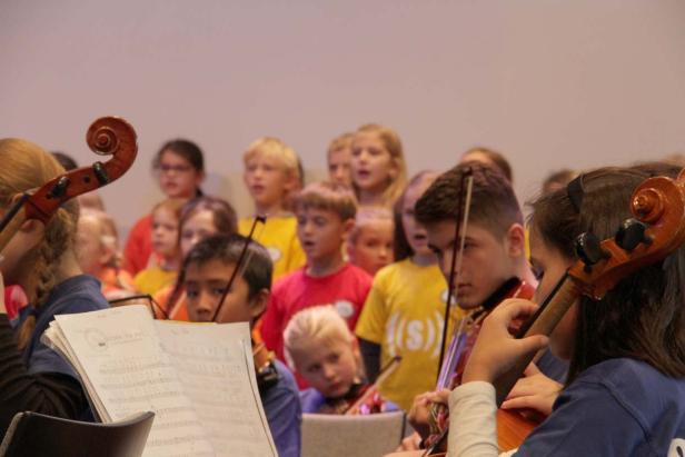 Ein Kinderorchester spielt und singt gemeinsam in einem hellen Raum.