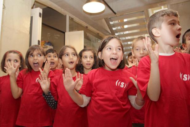 Eine Gruppe Kinder in roten T-Shirts singt oder ruft begeistert.