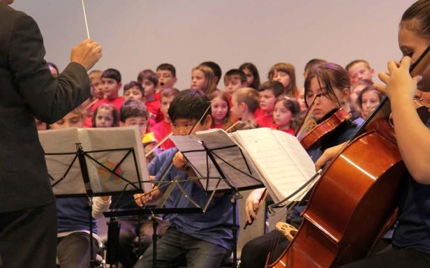 Ein Kinderorchester spielt unter der Leitung eines Dirigenten vor einem Chor.