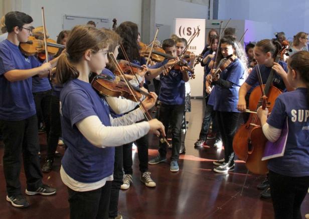 Eine Gruppe junger Menschen spielt in einem Orchester Geige und Cello.