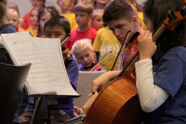 Ein Jugendorchester spielt Geige und Cello vor einem Publikum.