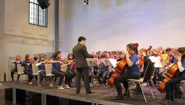 Ein Jugendorchester spielt unter der Leitung eines Dirigenten auf einer Bühne.