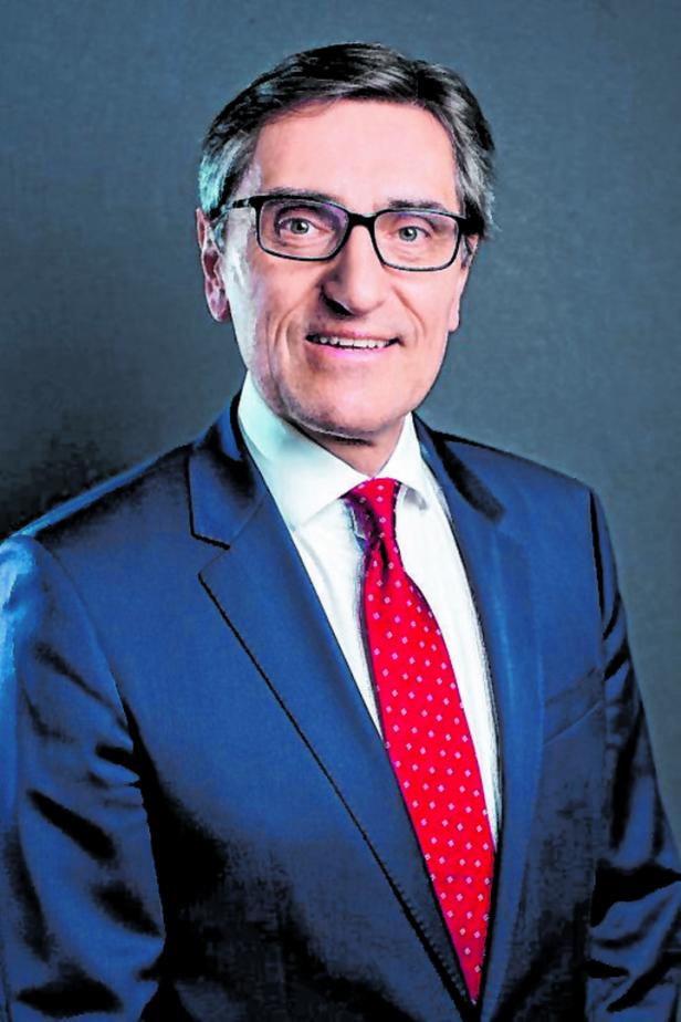 Ein Mann mit Brille, Anzug und roter Krawatte lächelt in die Kamera.