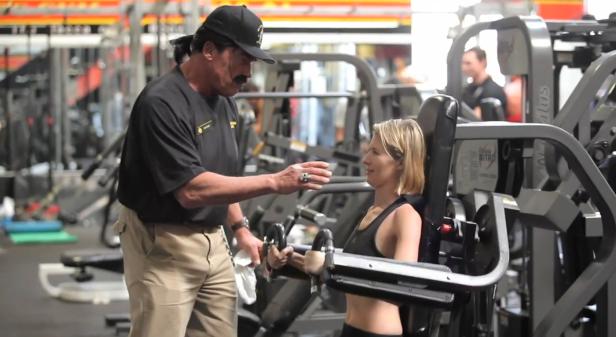 Ein Trainer hilft einer Frau an einer Krafttrainingsmaschine im Fitnessstudio.