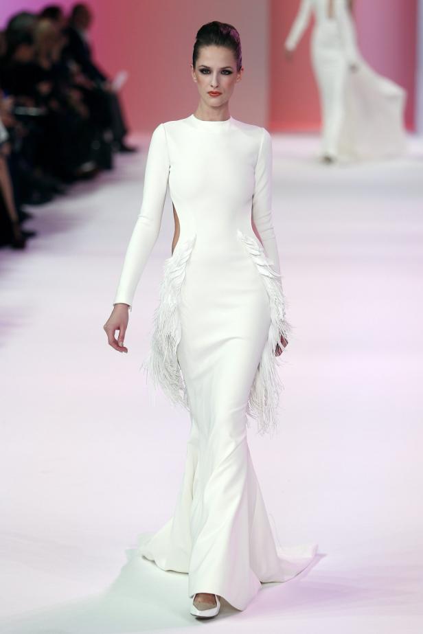 Eine Frau in einem langen, weißen Kleid mit Federn auf dem Laufsteg.