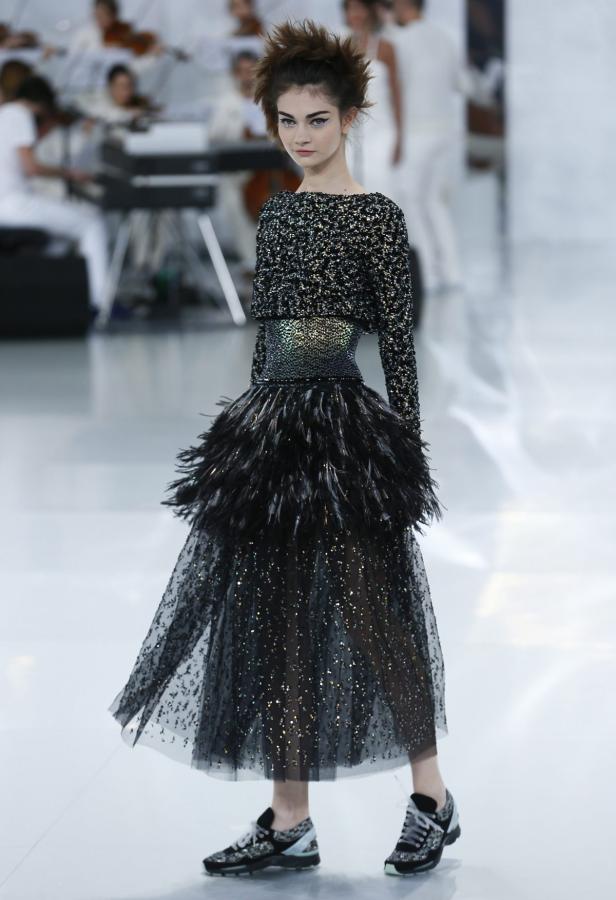 Ein Model präsentiert ein glitzerndes, gefiedertes Kleid und Turnschuhe auf dem Laufsteg.