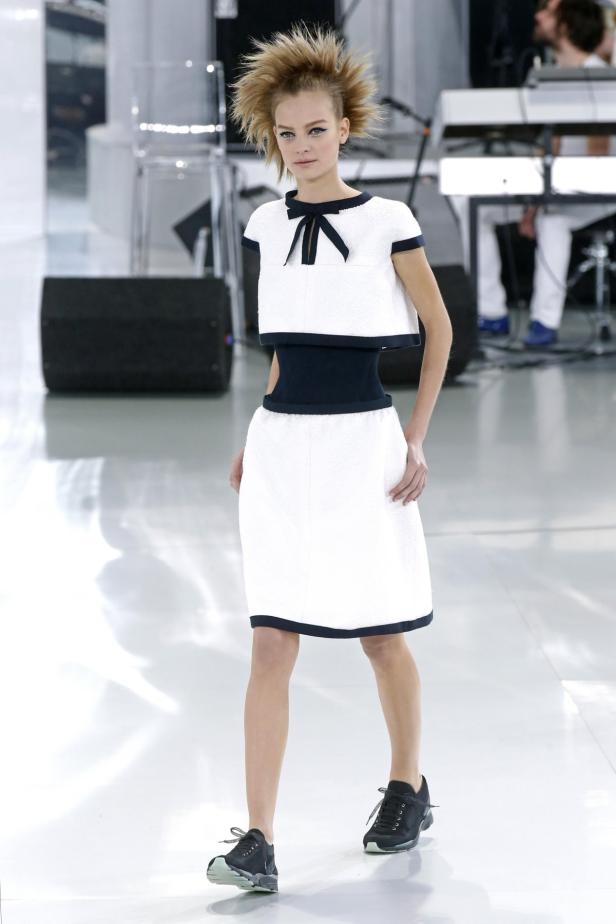 Ein Model mit weißem Kleid und Turnschuhen auf dem Laufsteg.