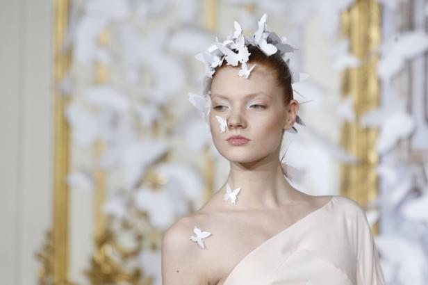 Eine Frau mit weißem Kleid und weißen Papier-Schmetterlingen im Haar und auf dem Körper.