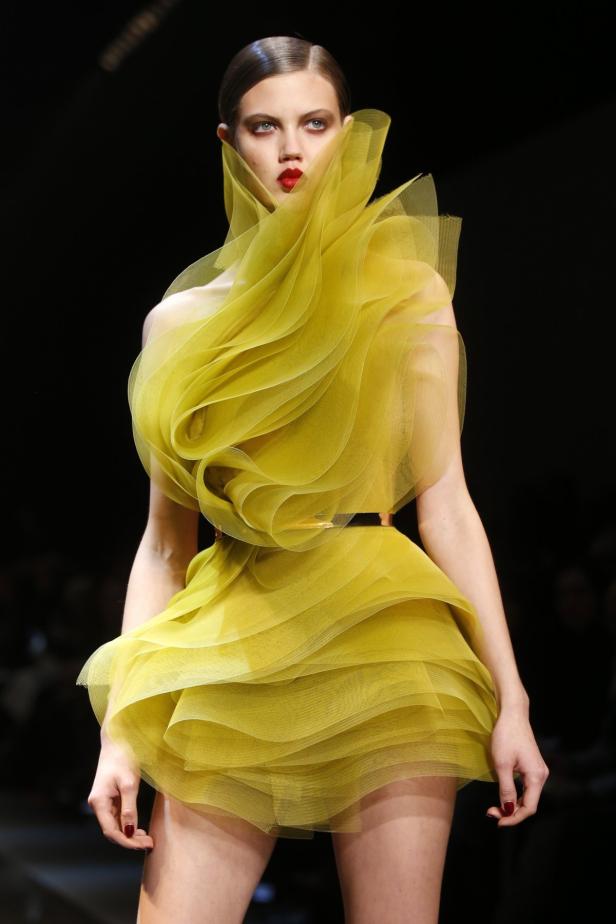 Ein Model präsentiert ein gelbes Kleid mit Rüschen auf dem Laufsteg.