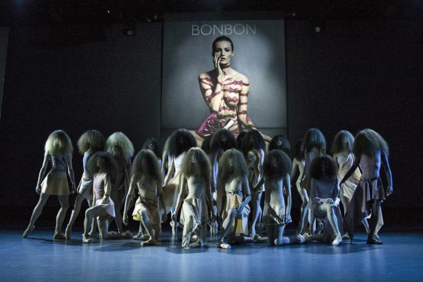 Eine Gruppe von Tänzern auf einer Bühne vor einem Plakat mit der Aufschrift „BONBON“.