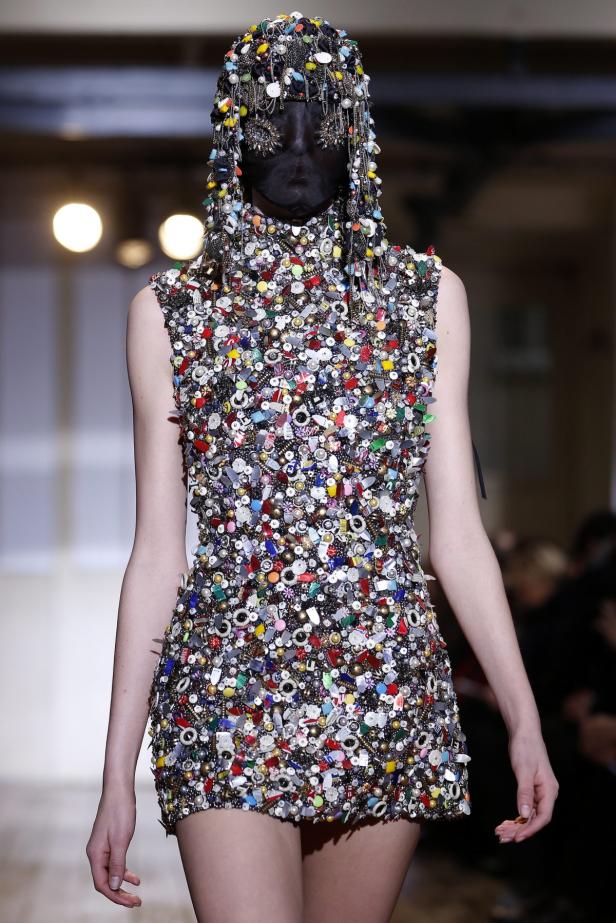 Ein Model trägt ein mit Knöpfen und Perlen besetztes Kleid und eine Kopfbedeckung mit Schleier.