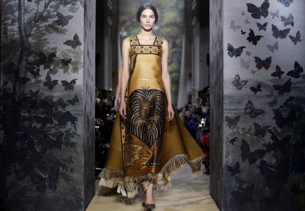 Ein Model präsentiert ein langes, braunes Kleid mit einem Löwenmotiv auf dem Laufsteg.