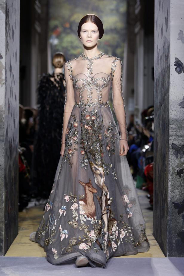 Ein Model präsentiert ein graues, transparentes Kleid mit floralen Stickereien und einem Hirschmotiv.