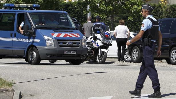 Ein Gendarm überquert eine Straße, im Hintergrund ein Polizeiwagen und ein Motorrad der Polizei.