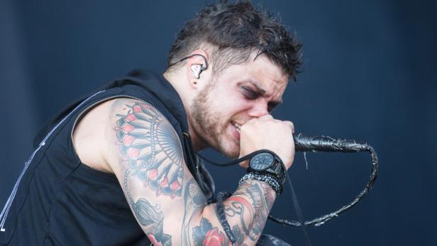 Ein Sänger mit Tattoos singt mit geschlossenen Augen in ein Mikrofon.