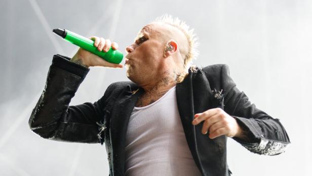 Ein Sänger mit Irokesenschnitt und Tattoos singt in ein grünes Mikrofon.
