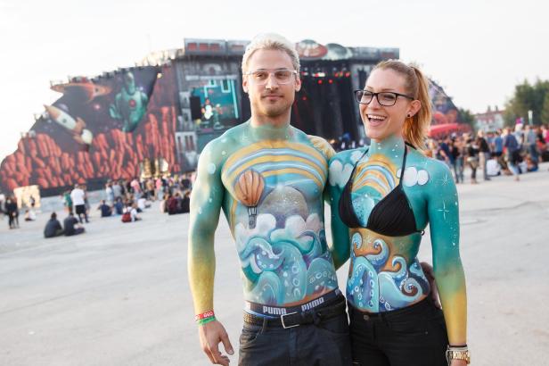 Ein Paar mit Körperbemalung posiert vor einer Festivalbühne.