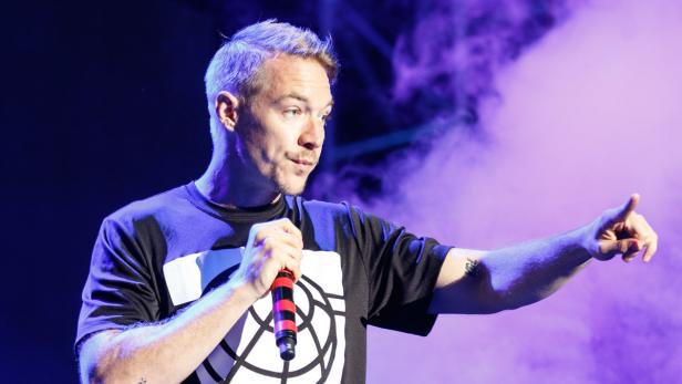Diplo hält ein Mikrofon und zeigt mit dem Finger auf der Bühne.