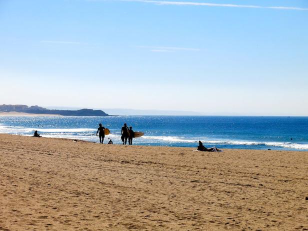 Surfer gehen an einem sonnigen Tag am Strand entlang.