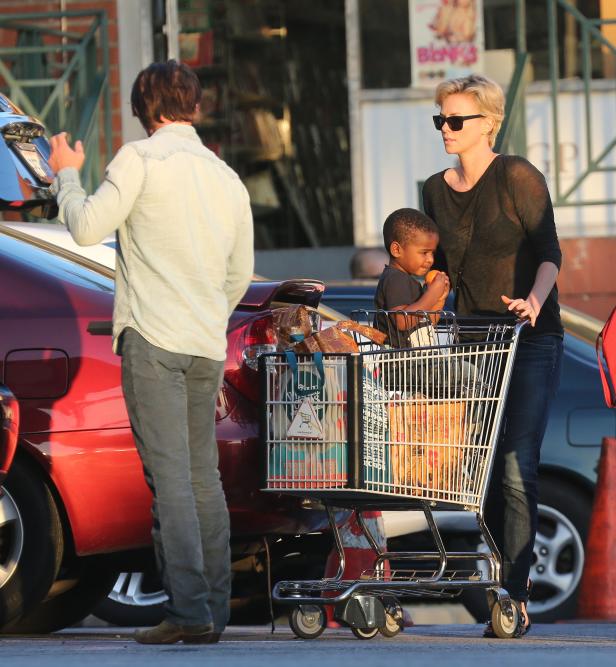 Charlize Theron mit Kind und Einkaufswagen auf einem Parkplatz.