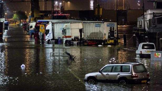 Überschwemmte Straße mit mehreren Lastwagen und Autos im Wasser.