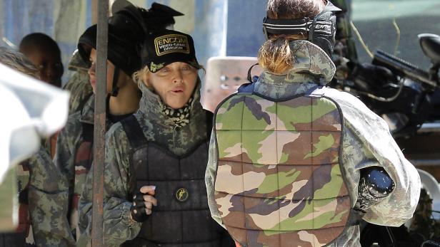 Madonna nimmt an einem Paintball-Spiel mit Schutzkleidung und einer „Encom Video Game Division“-Kappe teil.