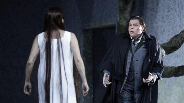 Eine Szene aus einer Opernaufführung mit einer Frau im weißen Kleid und einem Mann im Anzug.