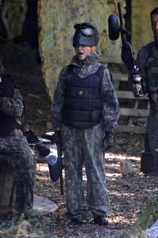 Eine junge Person in Tarnkleidung und mit Paintball-Ausrüstung steht auf einem Feld.