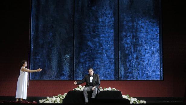 Auf einer Bühne sitzen ein Mann im Anzug und eine Frau im weißen Kleid vor einer blauen Wand.