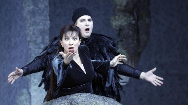 Eine Frau mit blutverschmiertem Mund und ein Mann in einem Federkostüm treten in einer Oper auf.