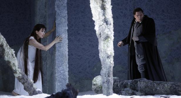 Eine Frau im weißen Kleid und ein Mann im Mantel stehen auf einer Bühne mit Eisdekor.