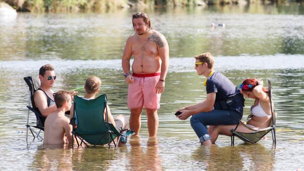 Eine Gruppe von Menschen sitzt und steht im Wasser an einem sonnigen Tag.