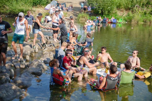 Eine Gruppe von Menschen sitzt und steht in einem Fluss, einige trinken Getränke.