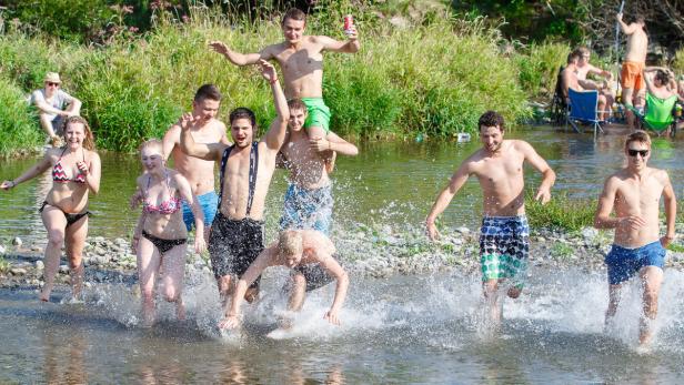 Eine Gruppe junger Leute watet und planscht in einem Fluss an einem sonnigen Tag.