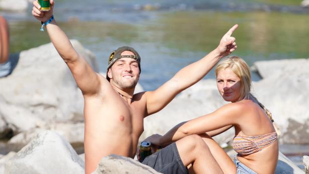 Ein Mann und eine Frau sitzen mit Getränken an einem Fluss.