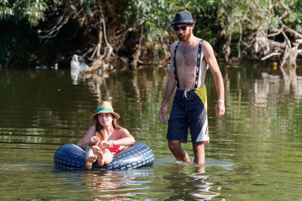 Eine junge Frau treibt auf einem Reifen im Wasser, während ein Mann durch das Wasser watet.
