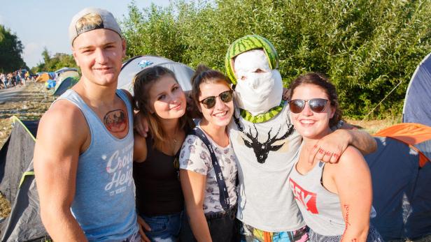 Eine Gruppe junger Leute posiert auf einem Campingplatz, einer trägt einen Melonenhelm.