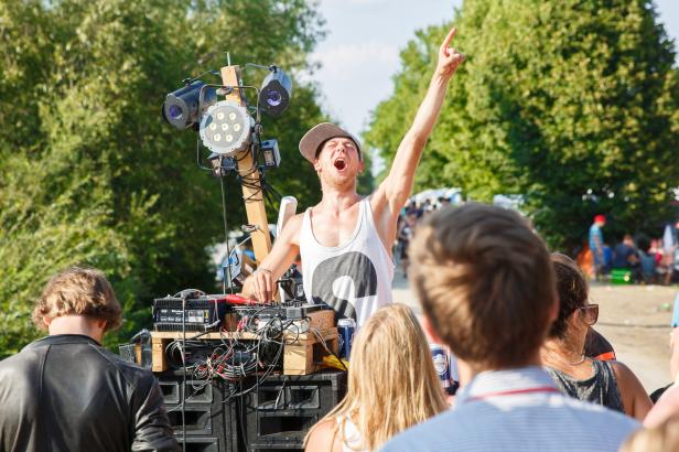 Ein DJ legt auf einer Open-Air-Veranstaltung vor einer jubelnden Menge auf.