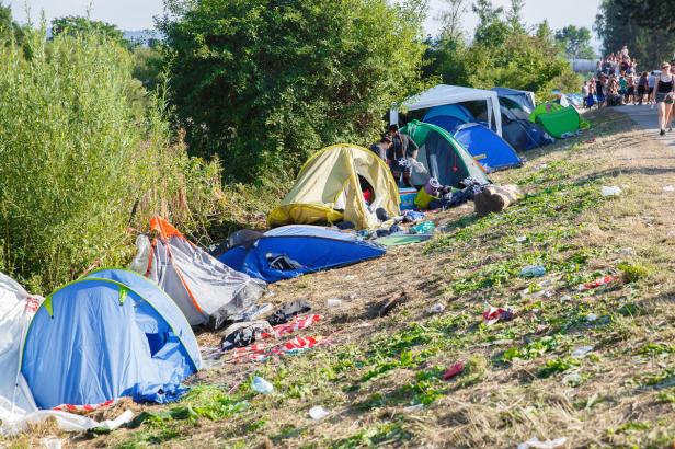 Mehrere Zelte stehen auf einem grasbewachsenen Hügel, übersät mit Müll.