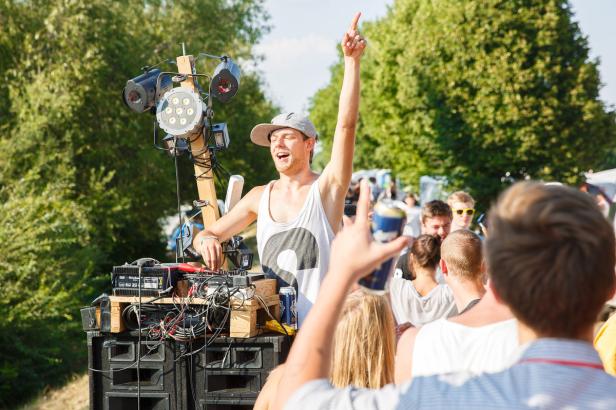 Ein DJ legt im Freien vor einer tanzenden Menge auf.