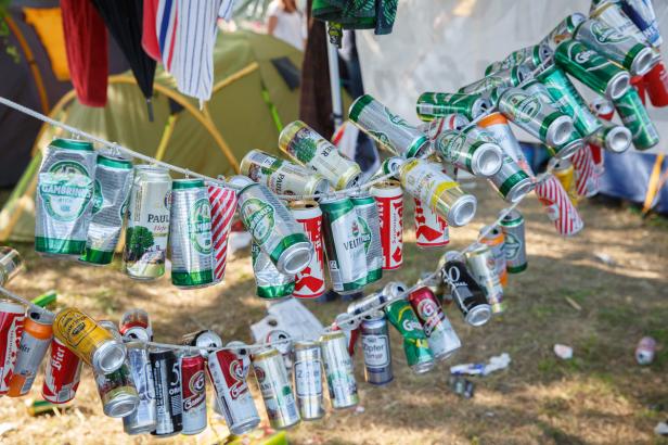 Auf einer Leine hängen leere, zerdrückte Bierdosen verschiedener Marken vor einem Zelt.