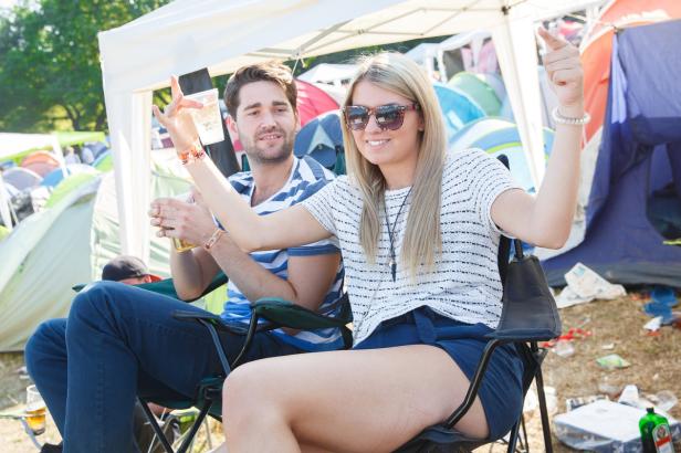 Ein junges Paar sitzt auf einem Campingplatz und prostet mit Getränken zu.