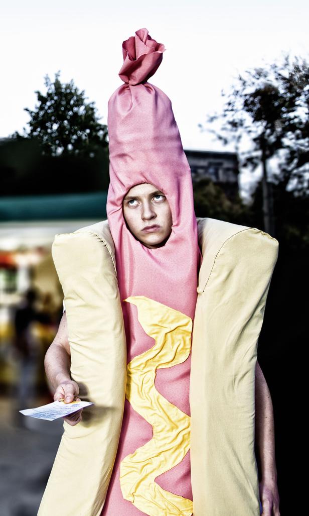 Eine Person in einem Hotdog-Kostüm hält einen Zettel in der Hand.
