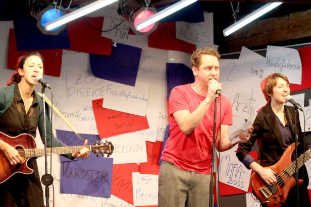 Drei Musiker treten vor einer Wand mit beschrifteten Zetteln auf.