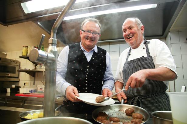 Zwei Köche bereiten in einer Küche Frikadellen zu.