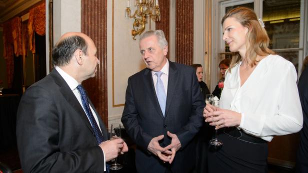 Drei Personen unterhalten sich bei einem formellen Anlass mit Champagnergläsern.