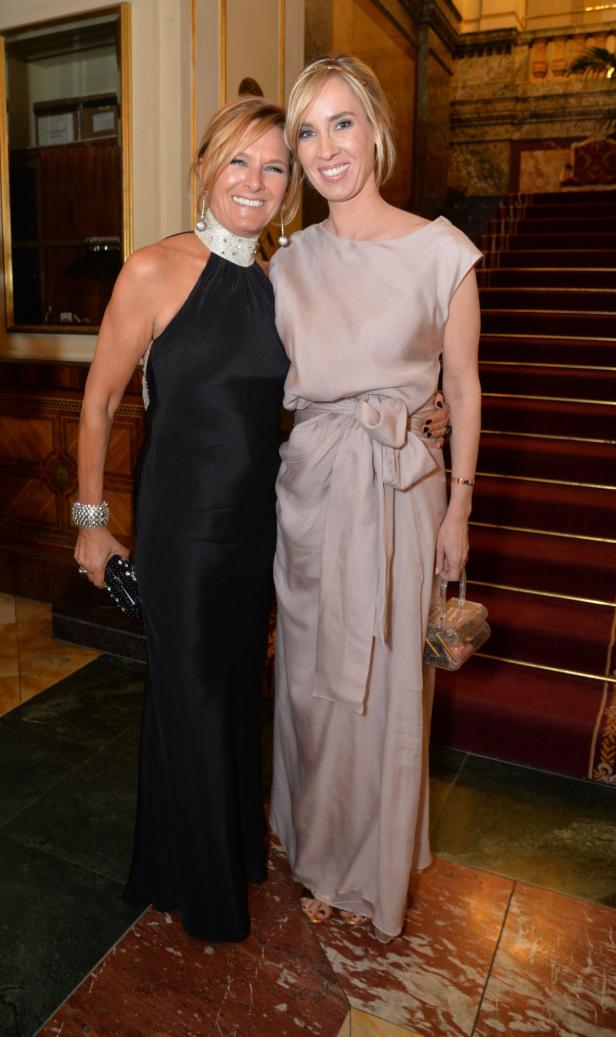 Zwei Frauen posieren in eleganten Abendkleidern vor einer Treppe.
